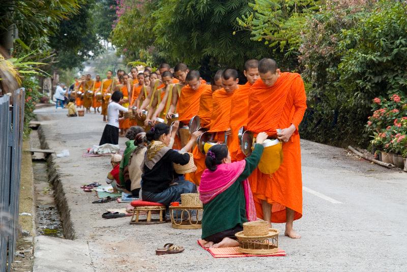 Photo Moines bouddhistes theravadans sur les aumônes traditionnelles du matin avec des habitants agenouillés plaçant la nourriture dans les bols des moines