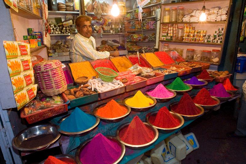 Photo Trader on colourful market stall (selling pigments and kumkum powder, incense, oil lamps etc. for Hindu worship) at night, Devaraja Market, Mysore, Karnataka, India 