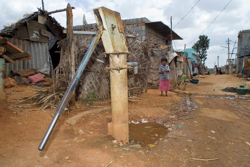 Photo Enfant à la pompe à eau manuelle dans la rue dans la réinstallation des bidonvilles périurbains