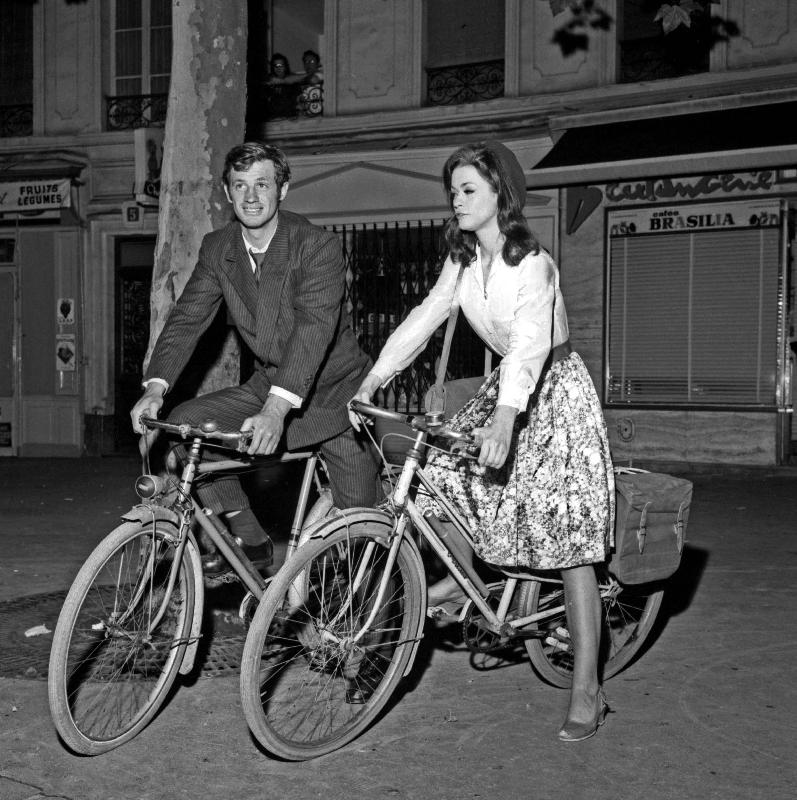 Photo Jean-Paul Belmondo et Marie Versini sur un vélo sur le tournage du film « Est-ce que Paris brûle ? » , 19 juillet 1965